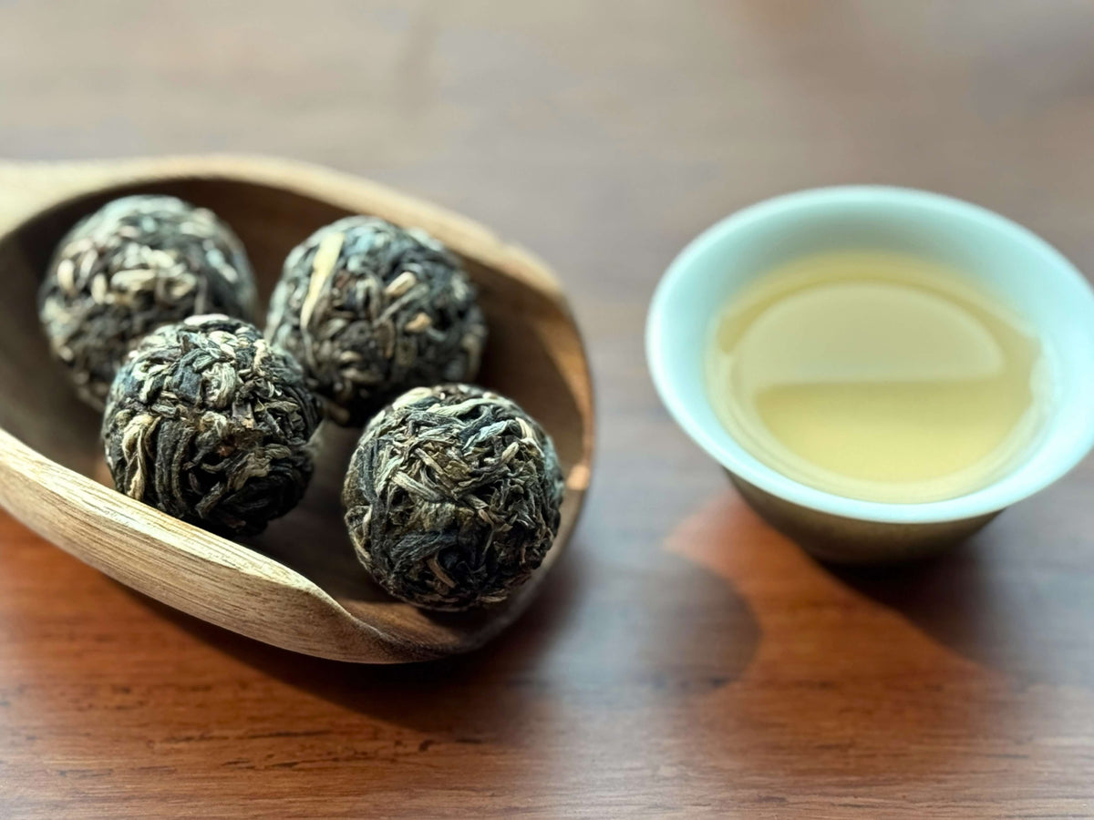 Puer balls in a wooden spoon on a brewing tray next to a cup of raw puer